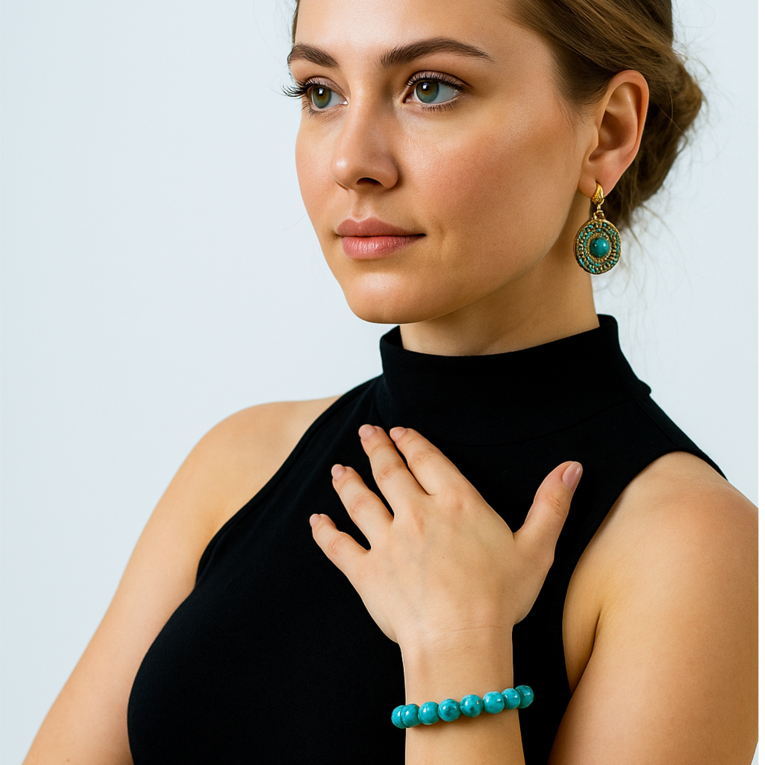 Woman wearing turquoise earrings and bracelet against a light gray background